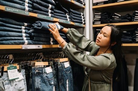 Ethical Clothing - Woman Looking at the Jeans on a Wooden Shelf