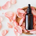 Essential Wardrobe. - Top view of empty brown bottle for skin care product placed on wooden plate with fresh pink rose petals on white background isolated