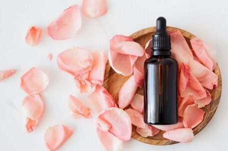 Essential Wardrobe. - Top view of empty brown bottle for skin care product placed on wooden plate with fresh pink rose petals on white background isolated