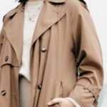 Chic Outerwear - Low angle of confident stylish young female with dark hair in trendy coat standing on street with hands in pockets and looking at camera